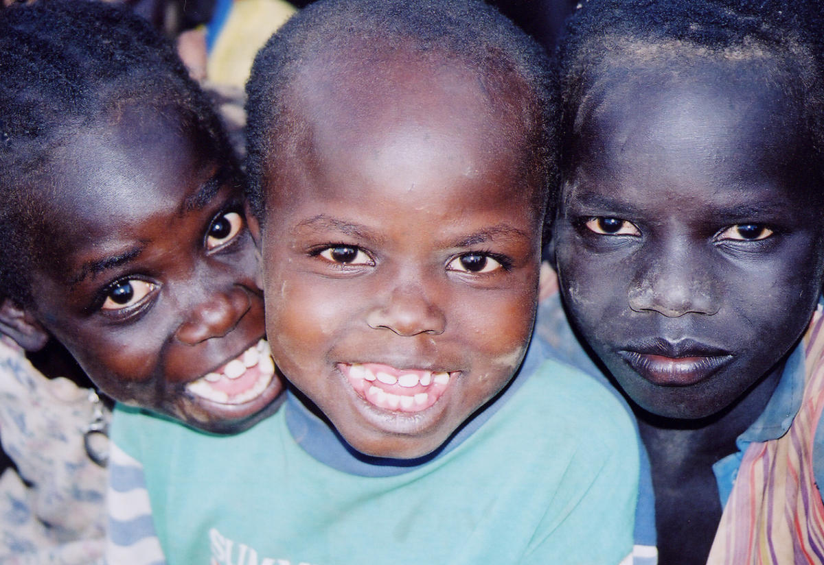 Three refugee boys, known as the "Lost Boys," pose for a photo together--two smiling, one with a serious expression