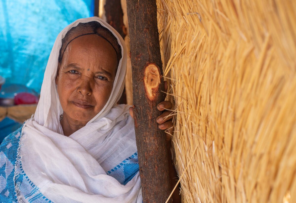 60-year old Berhan leans on a post under a thatched roof