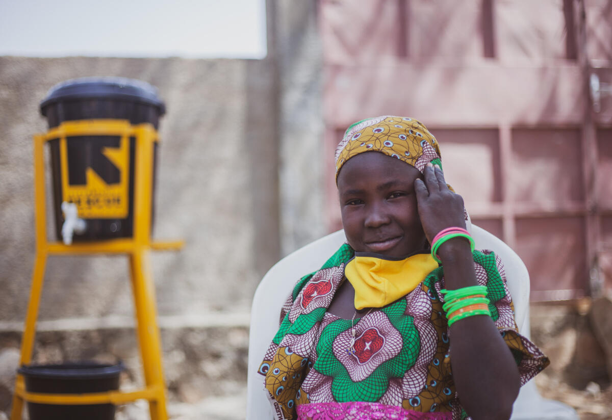 10-year old Anastasie from Cameroon dreams of becoming a teacher. Ten-year old Anastasie sits outside with elbow leaning on chair and her COVID-19 face mask pulled down around her neck.