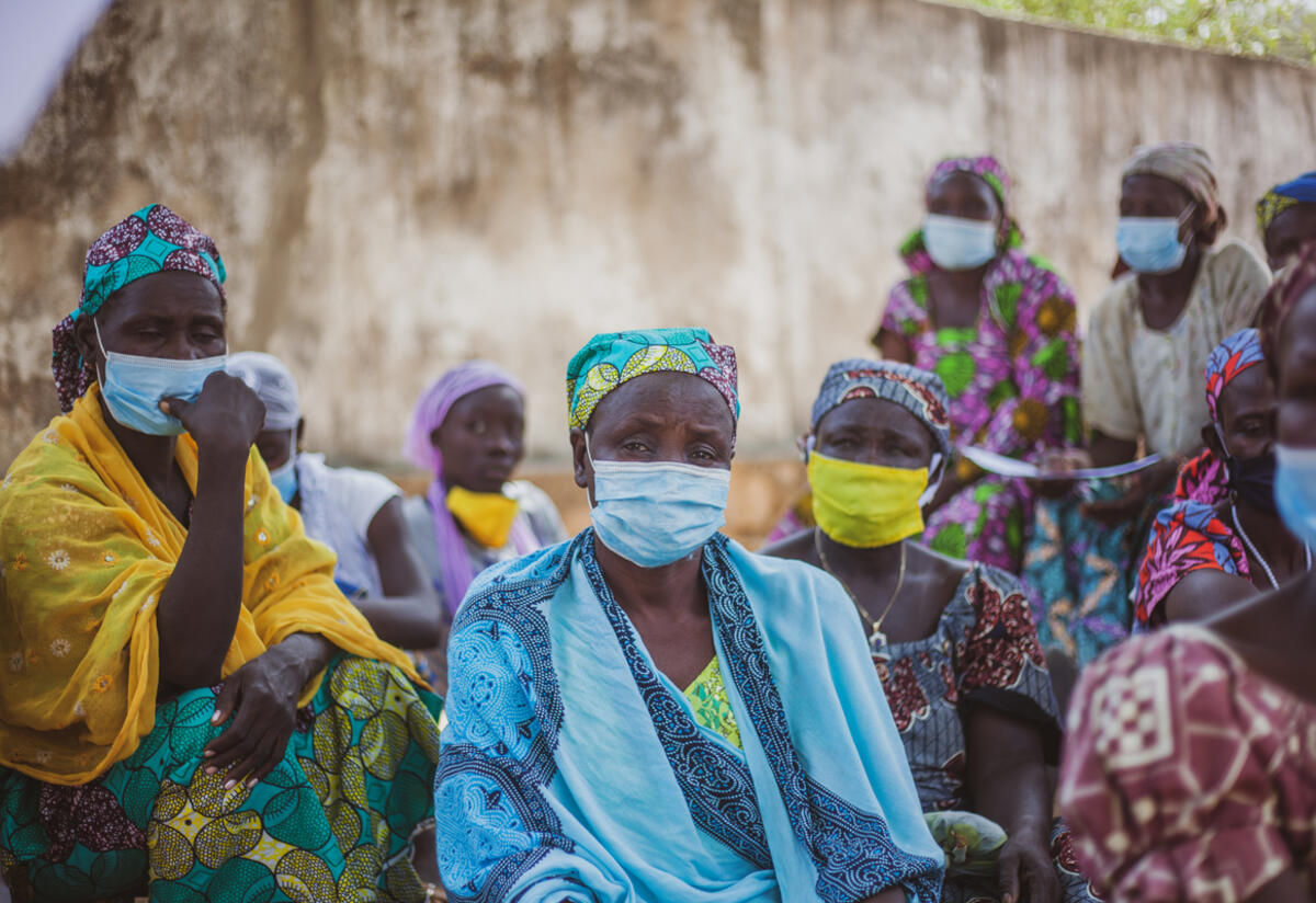 54-year-old Zara Tapita sits outdoors surrounded by other parents at an IRC Safe Space for children in Cameroon.