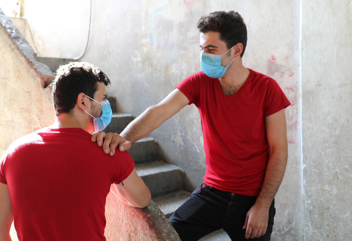 21-year-old Barakat, a Syrian refugee in Lebanon, stands on a stair wearing a mask with his hand on the shoulder of his brother Mohammed. They are wearing matching shirts. 