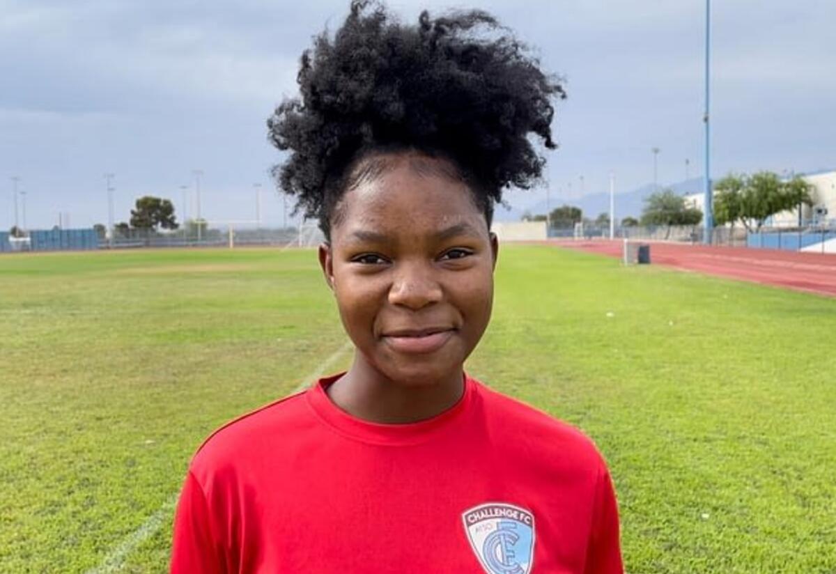 Kezia playing soccer Wearing a red shirt and smiling, Kezia looks at the camera while on a soccer field