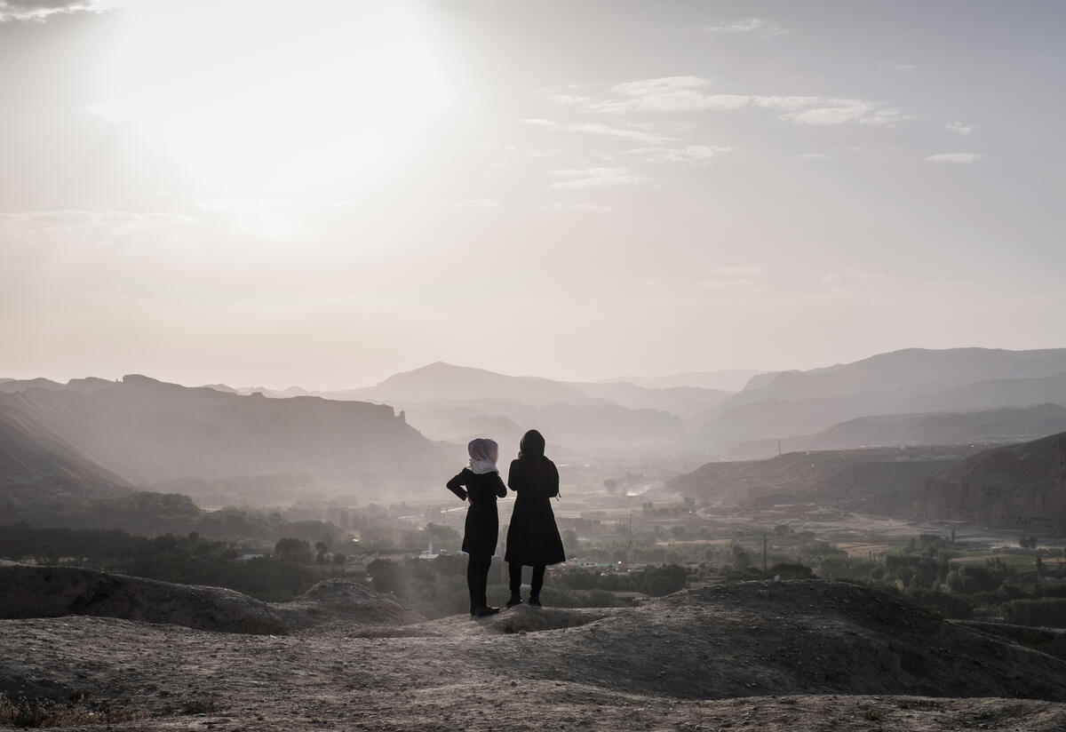 Two Afghan girls at the Shahr-e Gholghola ruin in Afghanistan A landscape photo with a mountainous landscape and the silhouettes of two girls who are looking at the landscape with their backs to the camera.