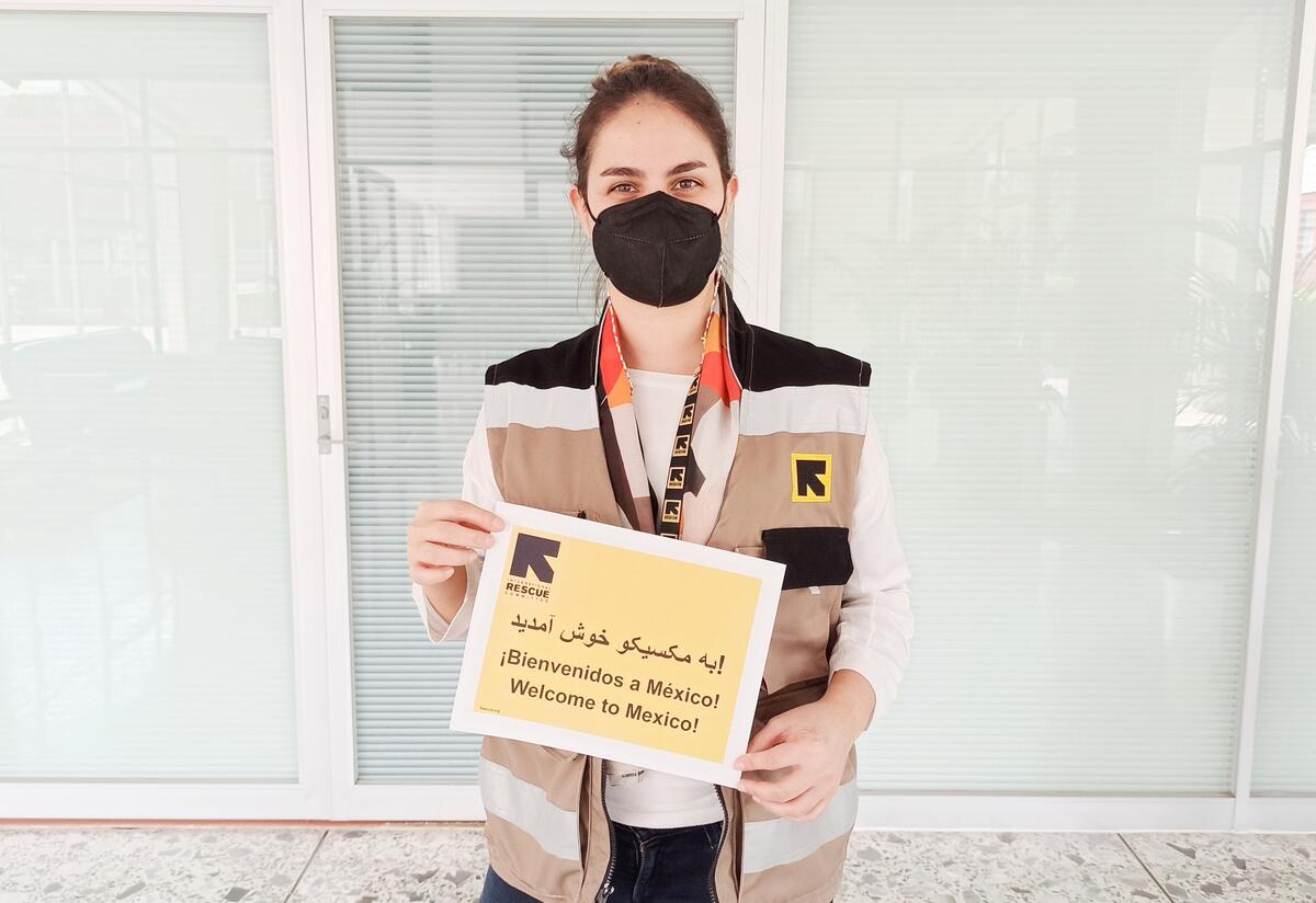 Fatima, a home visiting officer for the IRC in Mexico Fatima, a home visiting officer for the IRC in Mexico, holds a sign that says "welcome to Mexico" in English, Spanish and Dari. She is wearing a mask and an IRC vest.