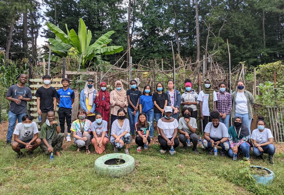 Photo of a ethnically diverse group of 30 high school students, all wearing masks, gathered in a community garden.