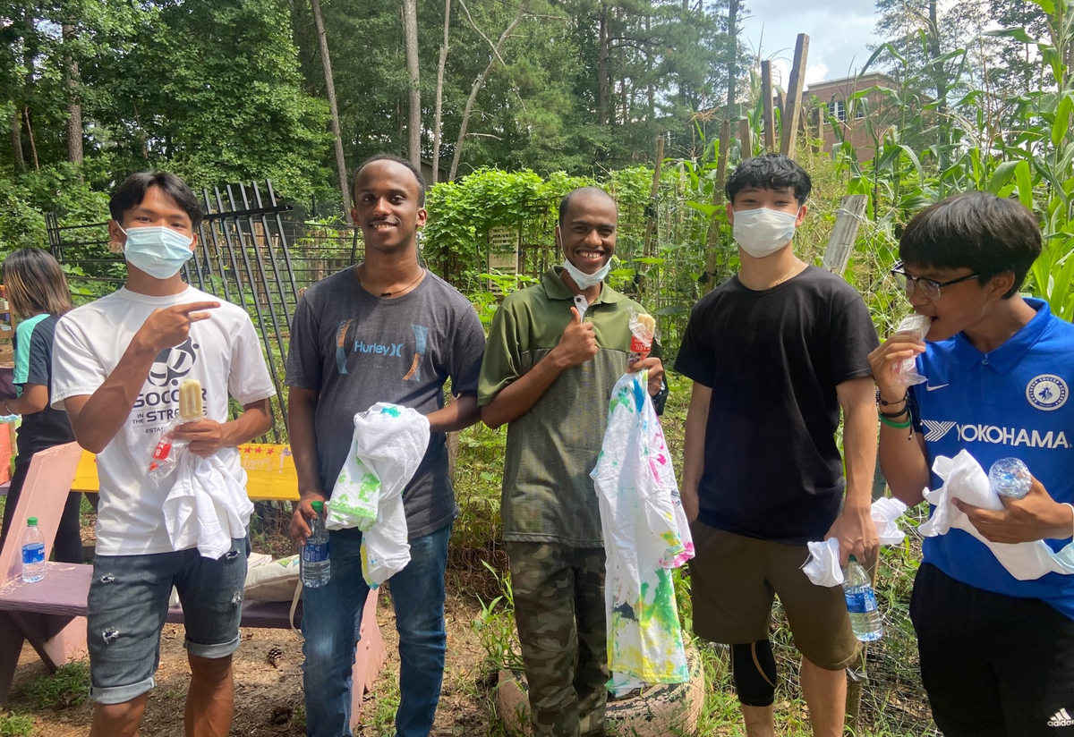 Summer Camp 21 King of Pops A group of 5 male high school students, 3 of Asian decent and 2 of African descent, standing in a community garden and eating popsicles.
