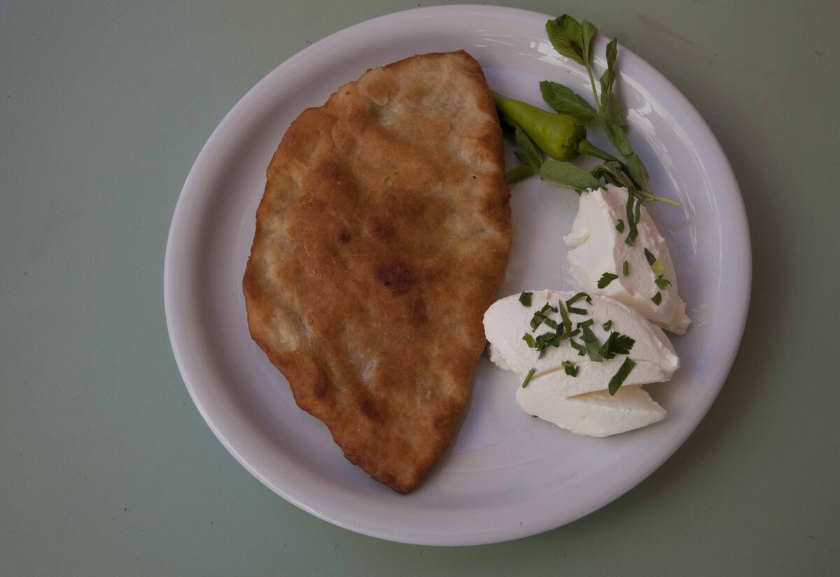 A dish of Afghan Bolani on a grey table. The dish consists of a fried piece of dough made of flour and potatoes, cheese and green herbs.  