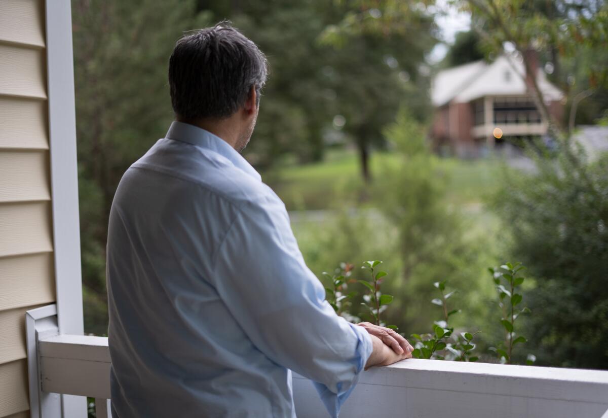 Afghan refugee Abdul, 52, stands alone on the porch of a friend's home in Virginia, looking out over the railing.