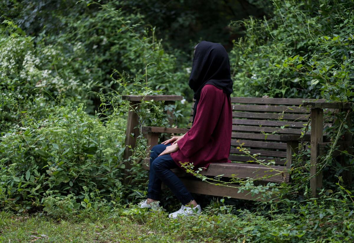 Afghan refugee Fatima, 19, sits facing sideways on a wooden garden swing in a lush garden in Richmond, VA