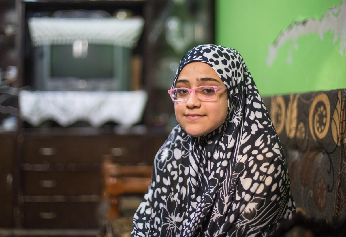 Salam, a 10-year-old Syrian girl wearing glasses, sits smiling for a photo.