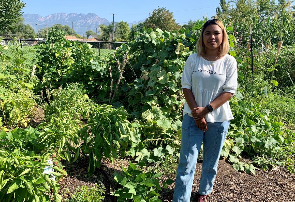 A woman stands next to the garden of produce she is growing.