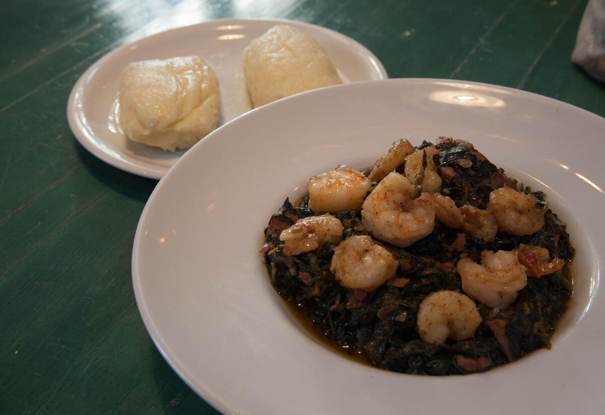 One plate with spinach and shrimp in the foreground, one plate with African fufu in the background.