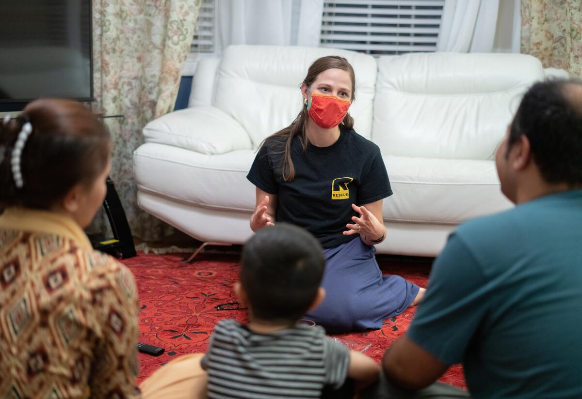 34-year-old Afghan translator Ali, is seen from behind seated on the floor with his wife and two young children as they speak with a female IRC staff member in Richmond, Virginia.