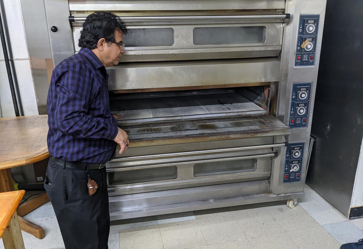 A storeowner standing next to a large oven.