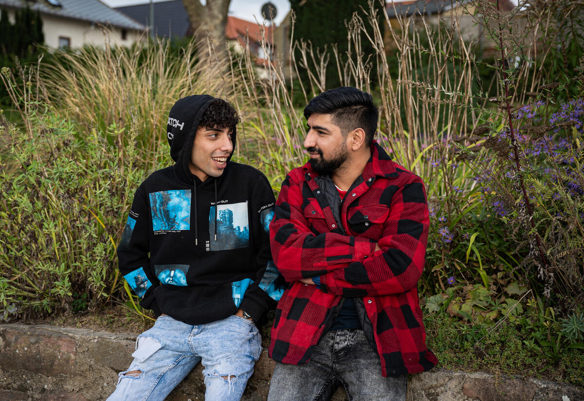 Afghan refugees Medhi and his teenage brother Ali, recently reunited in Germany, sit outside looking at each other and smiling as they talk.