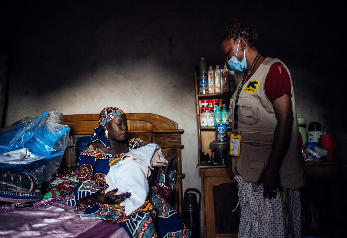 A Nigerian midwife watches over a woman and her baby, who is swaddled in a blanket
