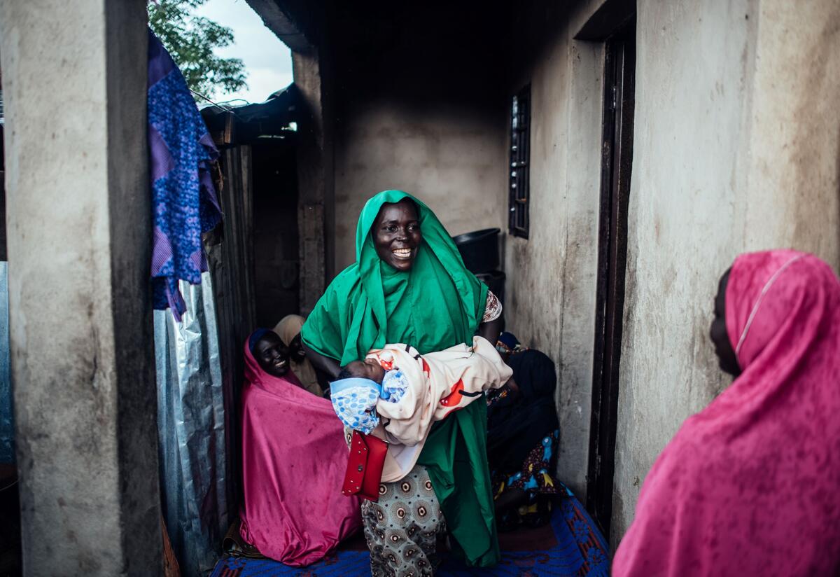 A Nigerian woman smiles and holds a baby who is swaddled in a blanket.