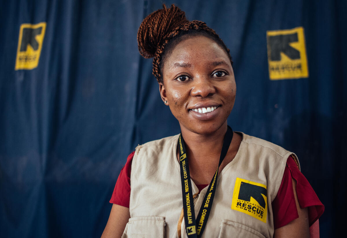 Murna, an IRC midwife in Nigeria Wearing an vest with an IRC logo, Murna looks at the camera and smiles.