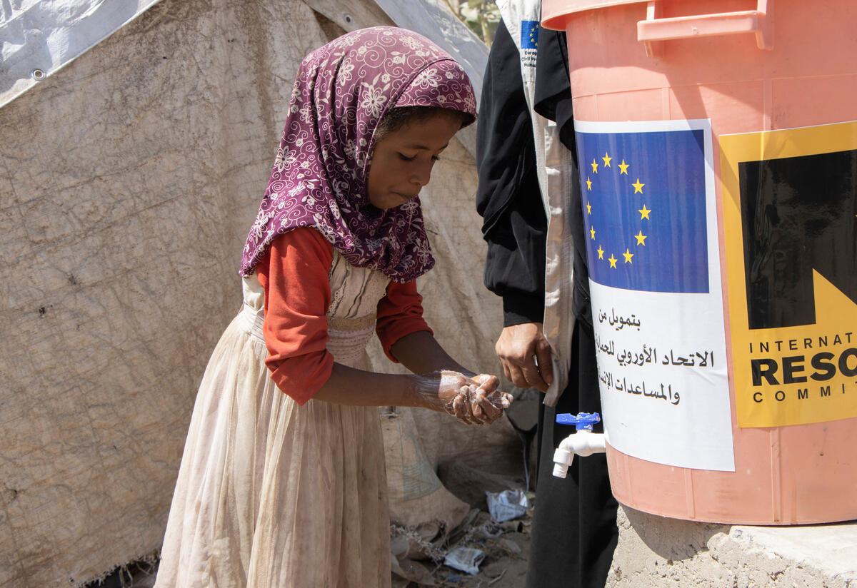 A Yemeni girl practices washing her hands at an outdoor tap as an IRC health worker looks on.