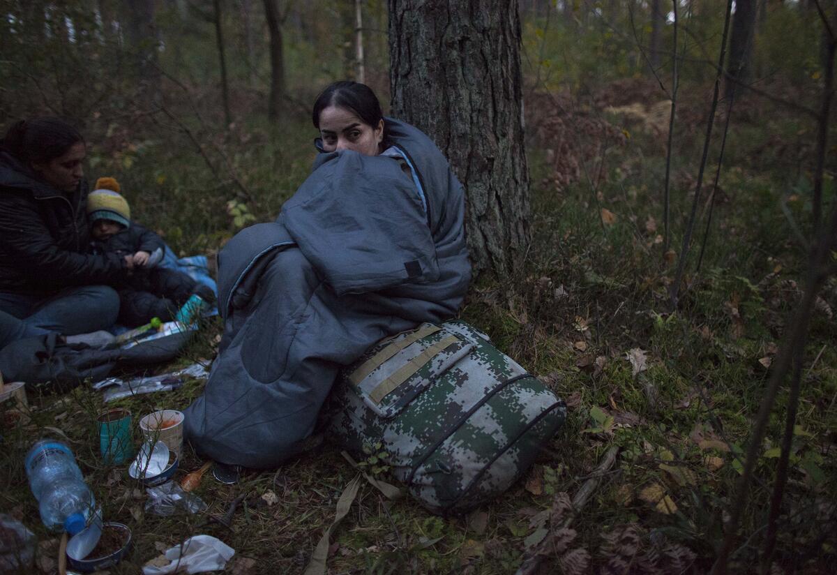 Kobieta, która niedawno przekroczyła granicę polsko-białoruską Kobieta siedzi na śpiworze po przekroczeniu granicy z Polską na Białoruś 6 października 2021 r. Jest w lesie, otoczona zapasami i wygląda na zmarzniętą.