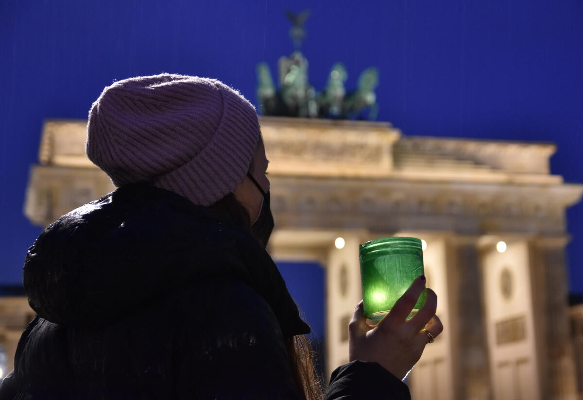 Kobieta stoi przed słynną Bramą Brandenburską trzymając małe zielone światło. 