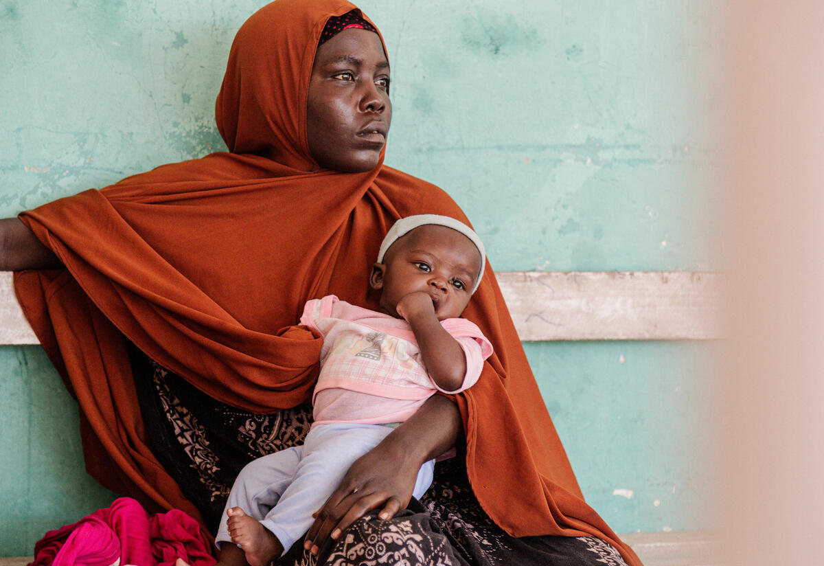 A mother in Somalia brings her child for nutrition support at an IRC clinic. A woman sits against a wall with her baby on her lap