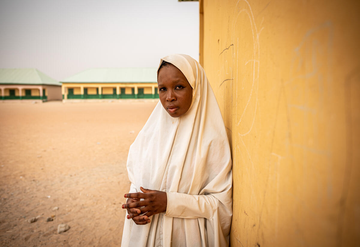An attendee at a European Union-funded IRC program for adolescents in conflict-affected northeast Nigeria. A young woman leans against the wall of a school building.