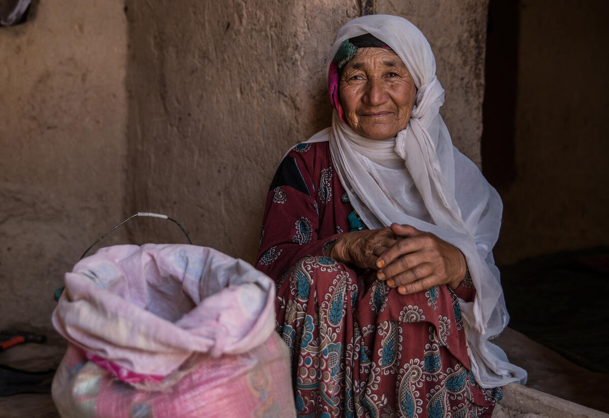 An older woman sits on the ground next to a bag of grain.