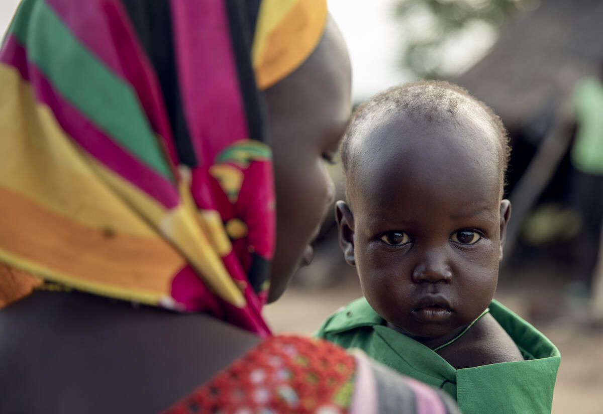 Abang holds her son Peter in South Sudan. They were displaced because of severe flooding Close up of a mother facing away from the camera while her baby faces toward the camera.