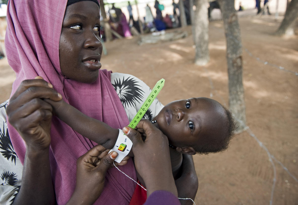 Mother holds child in displacement camp while undergoing medical tests
