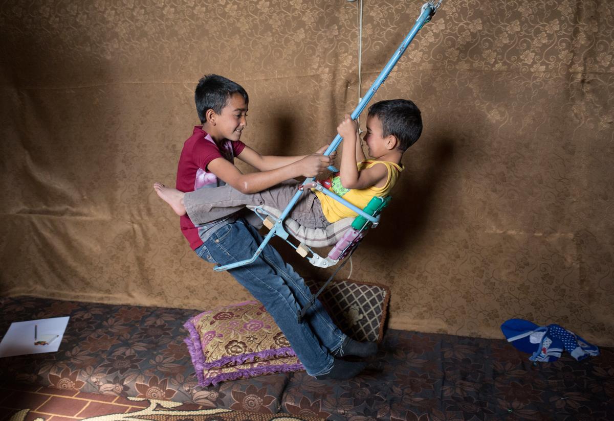 Two Syrian boys play on a homemade swing in their tent