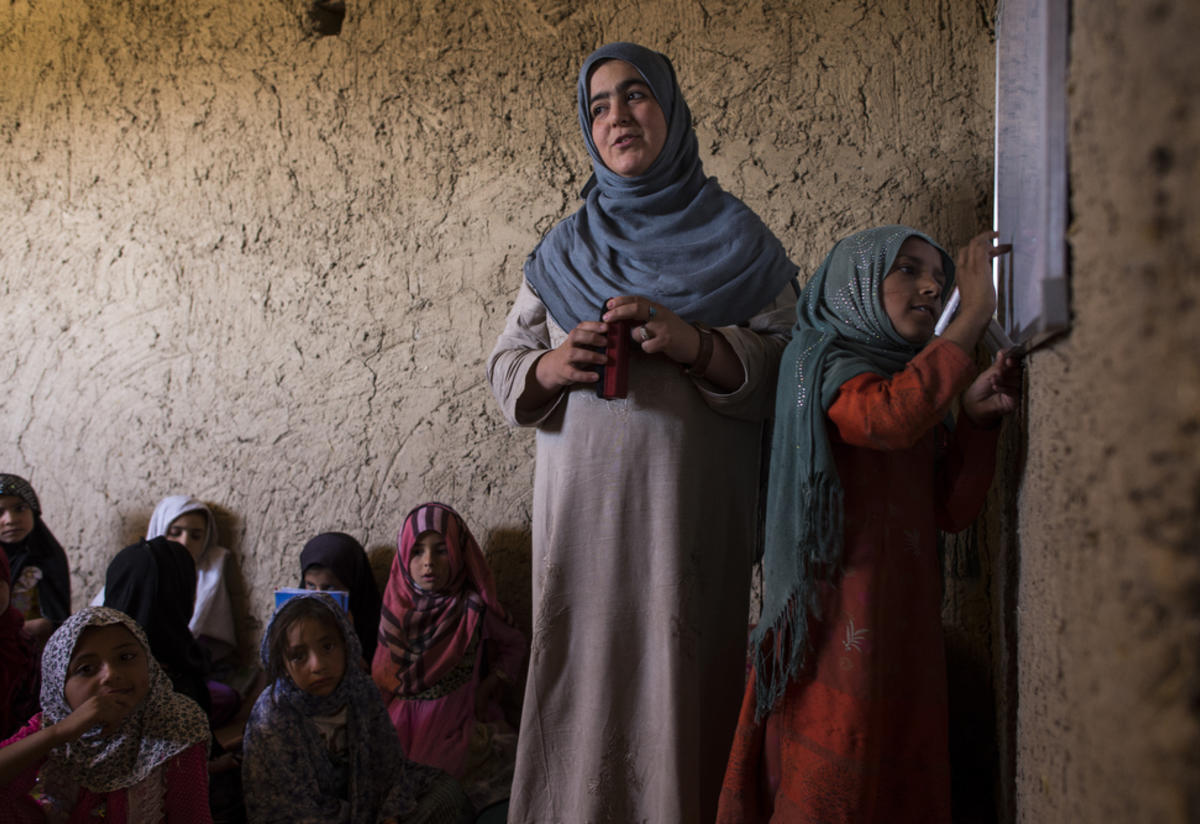 A teacher leads her class in an IRc-supported community school in Afghanistan A teacher leads her class in Afghanistan as a girl writes on the board