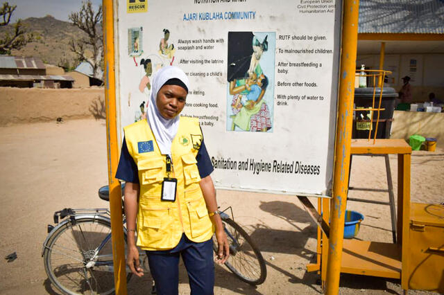 Aishatu in the field standing in front of a signboard