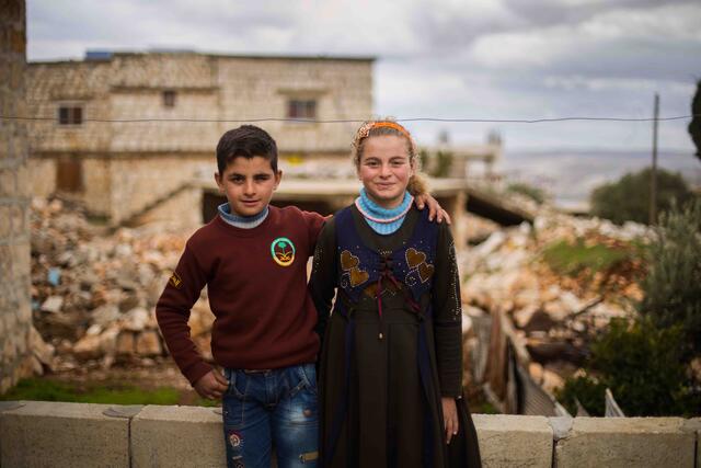Ten-year-old twins Aisha and Ali stand in front of their family's home which was damaged by an airstrike. 