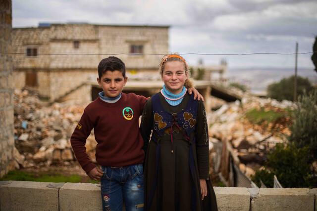 Ten-year-old twins Aisha and Ali stand in front of their family's home which was damaged by an airstrike.