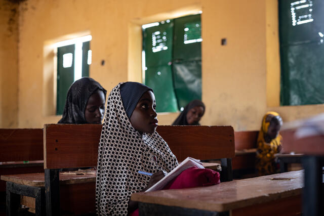 Fatima writing in her notebook whilst sat in a classroom.