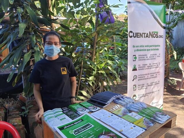 Chrisy stands outside at a desk with papers and leaflets on it and a pop up banner in the background