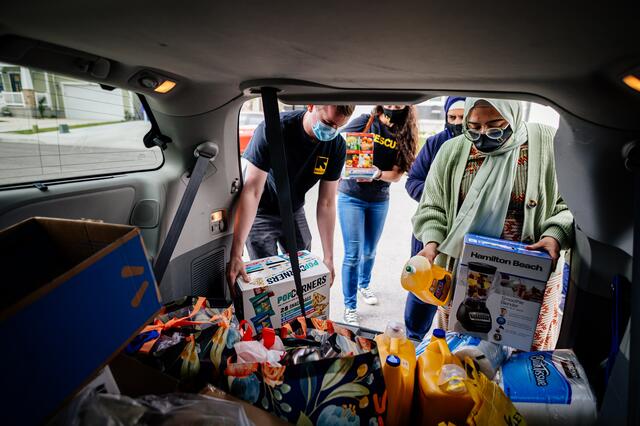 A trunk of a car is full of donations of household items, and IRC and Al-Mustafa foundation staff and volunteers are taking items to be delivered.