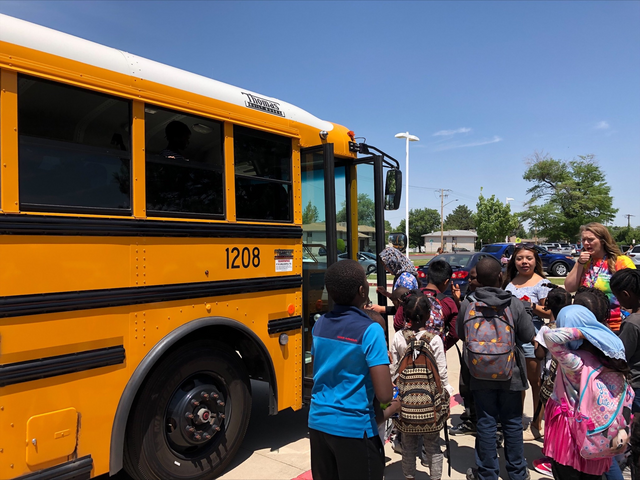 School children are being directed by a young woman in front of a school bus on a summer day