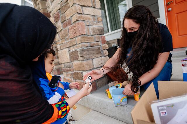 A woman kneels at the top of two steps, reaching out to hand a boy in his mother's arms a toy car provided by volunteers of the International Rescue Committee in Salt Lake City.
