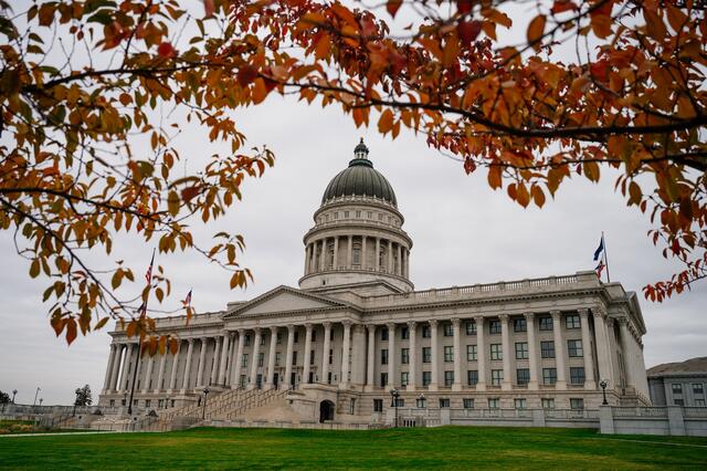 Utah State Capitol building framed with tree branches covered in leaves turned orange and yellow in autumn weather.