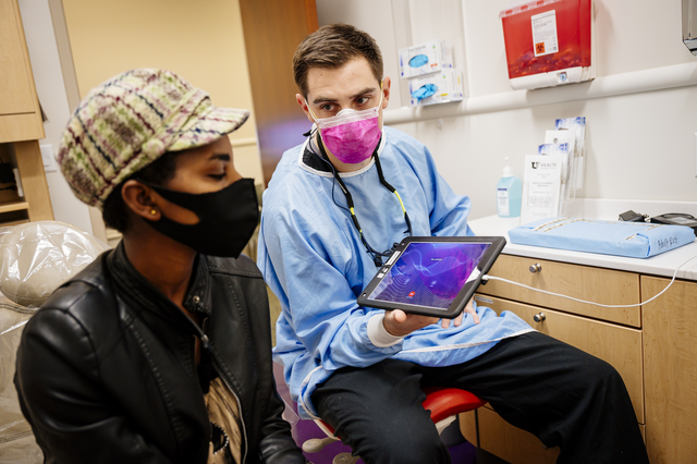 A doctor is showing a woman information on a tablet in a medical office, both are masked.