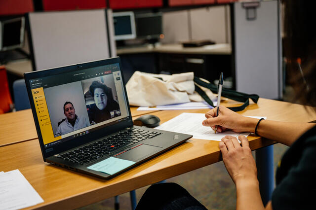 Person at a desk writing with a pen while on a Zoom call with two men. 