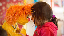 Ein kleines Mädchen legt ihre Stirn an eine Puppe der Sesamstraße und lächelt