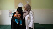 A female doctor stands beside a woman and her baby