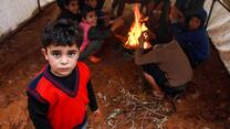 En pojke står vid en eld i Syrien och värmer sig