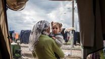 Eine syrische geflüchtete Mutter hält ihr Kind auf dem Arm in einer Zeltunterkunft.