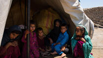 An Afghan family sits in the shade of an open tent