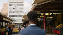 Moussa, a refugee from Ivory Coast, walks through a food market in Athens