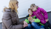 A mother sits with her son, daughter, and their family's cat.